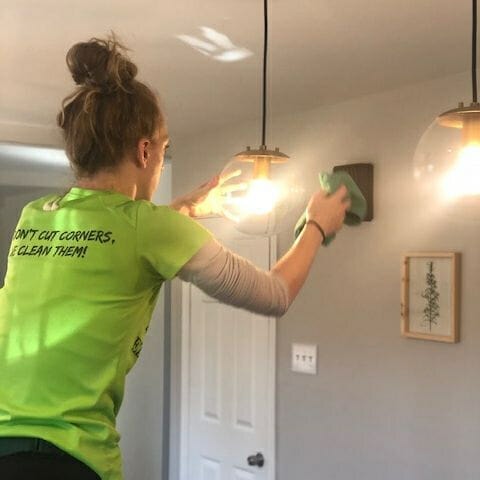 A woman cleaning a light fixture in a room.